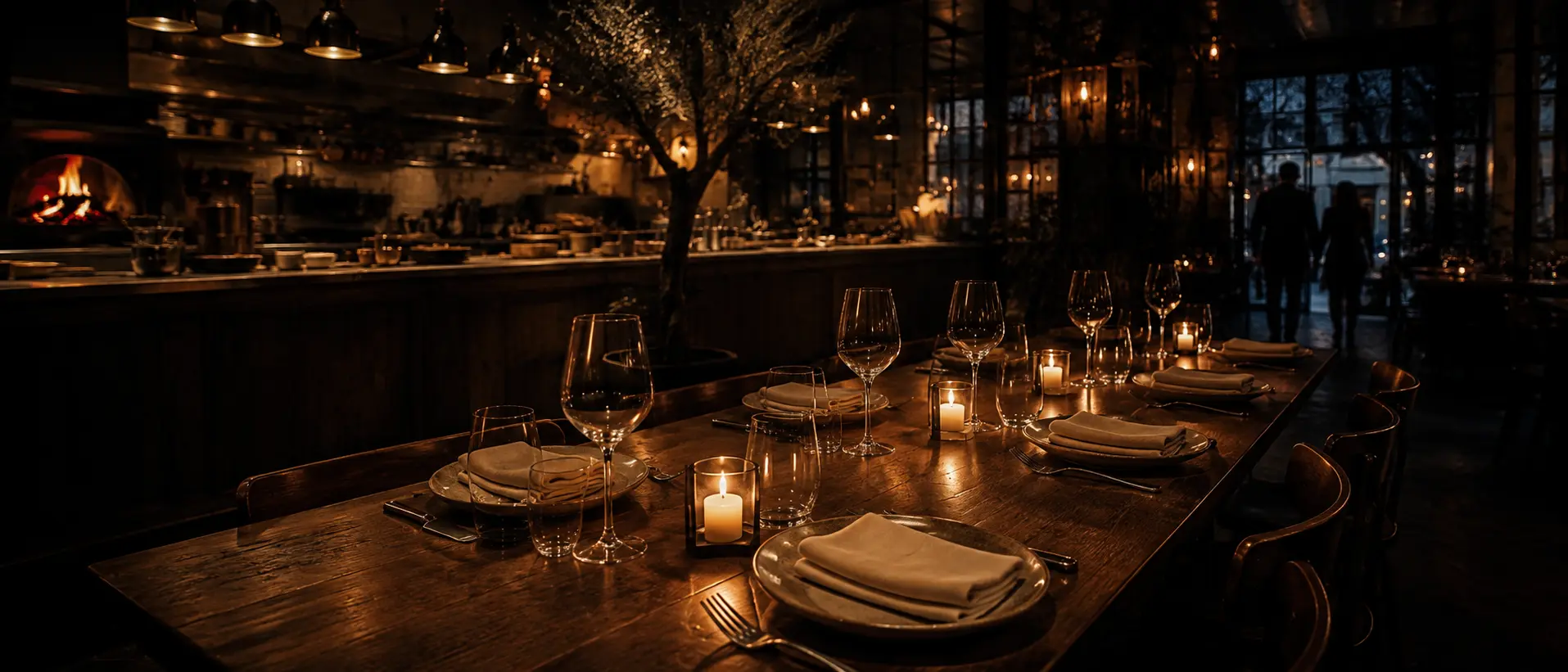Table dressée pour deux chez Ombra — bougies allumées, verres, bois foncé et lumière chaude sous les verrières noires